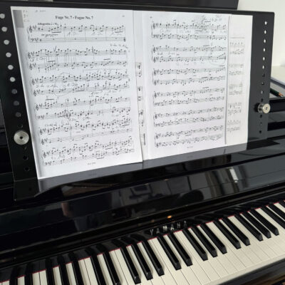 Notenblätter auf einem Notenständer, der auf einem Yamaha-Klavier steht, sichtbar sind mehrere Notenlinien und Schlüssel.